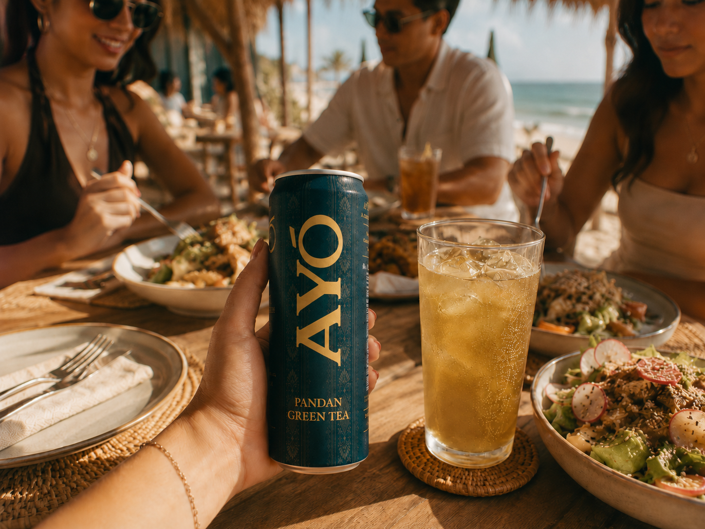 Hand holding a cold AYÓ Pandan Green Tea can at a beachside lunch