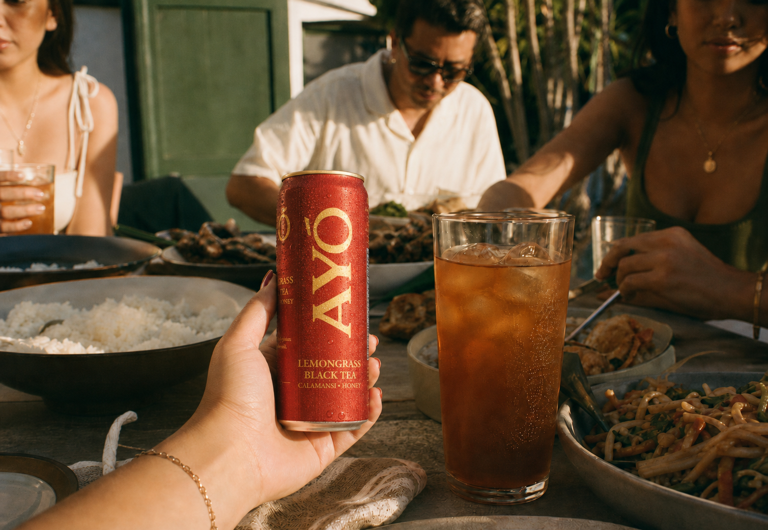 Hand holding a cold AYÓ Lemongrass Black Tea can at a Filipino dinner table